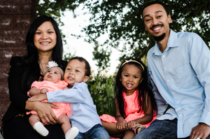 Family sitting outdoors against a brick wall backdrop wearing coordinated coral and blue outfits.