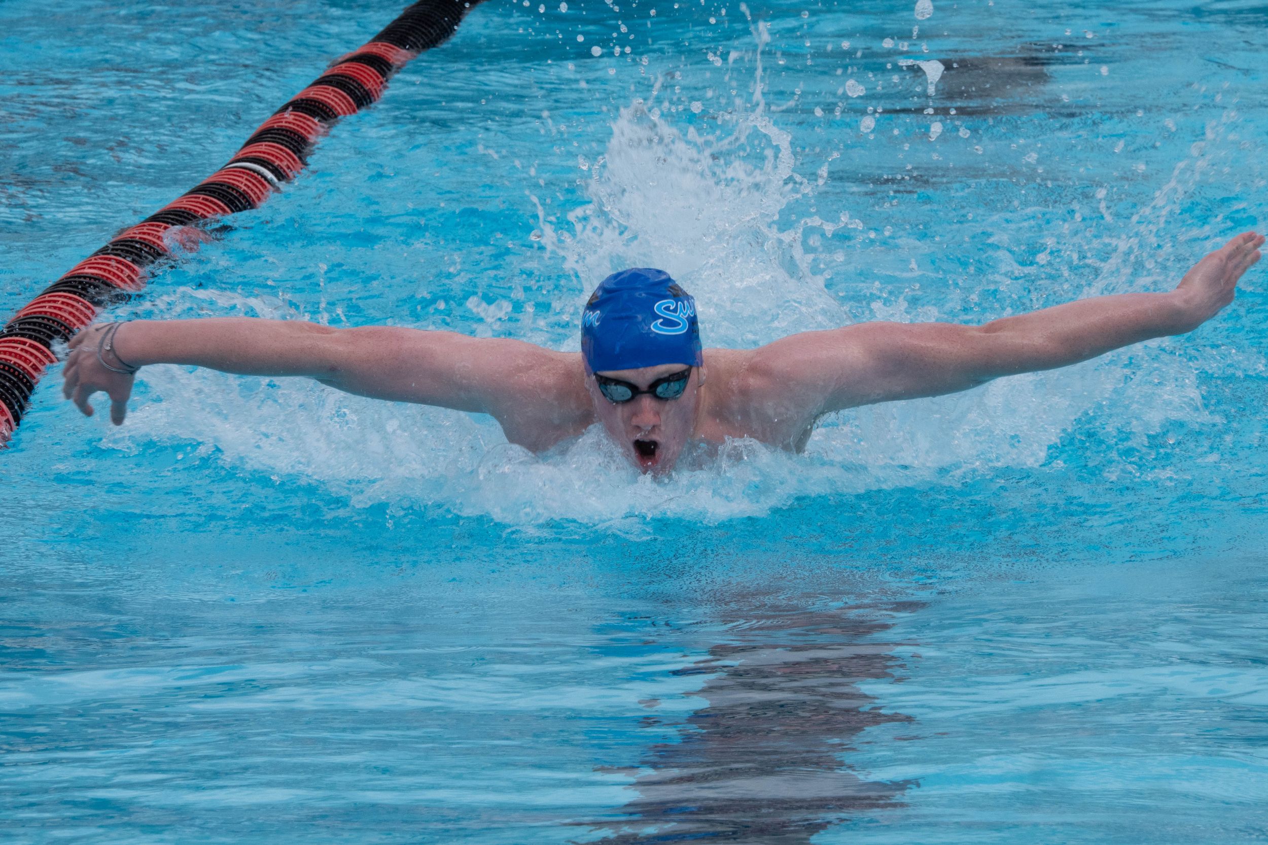 A swimmer performs the butterfly stroke in a swimming pool with red lane dividers and blue water.
