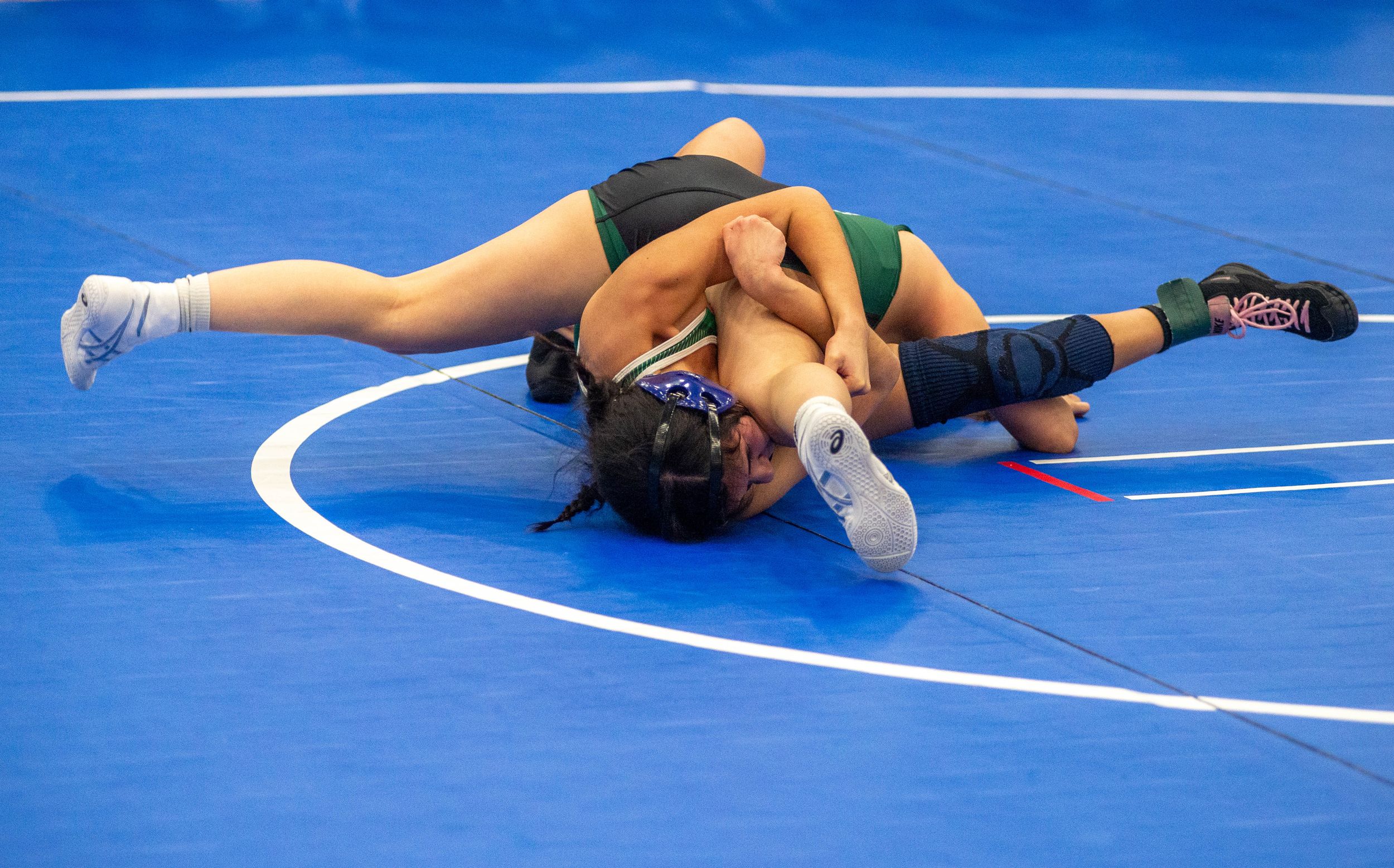 Two female wrestlers compete on a blue mat, with one athlete pinning her opponent during a wrestling match.