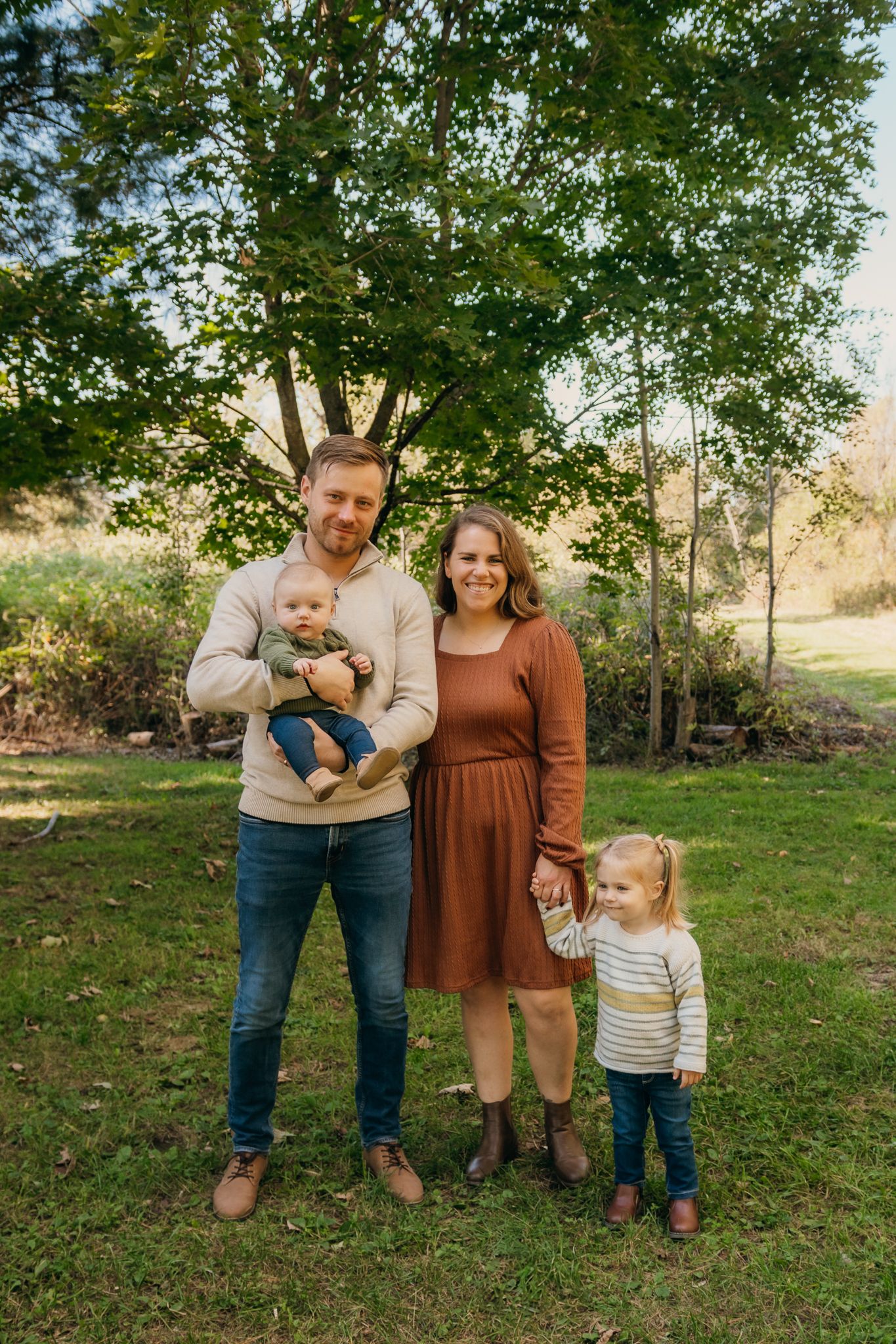 A family of four standing together with a large tree behind them.