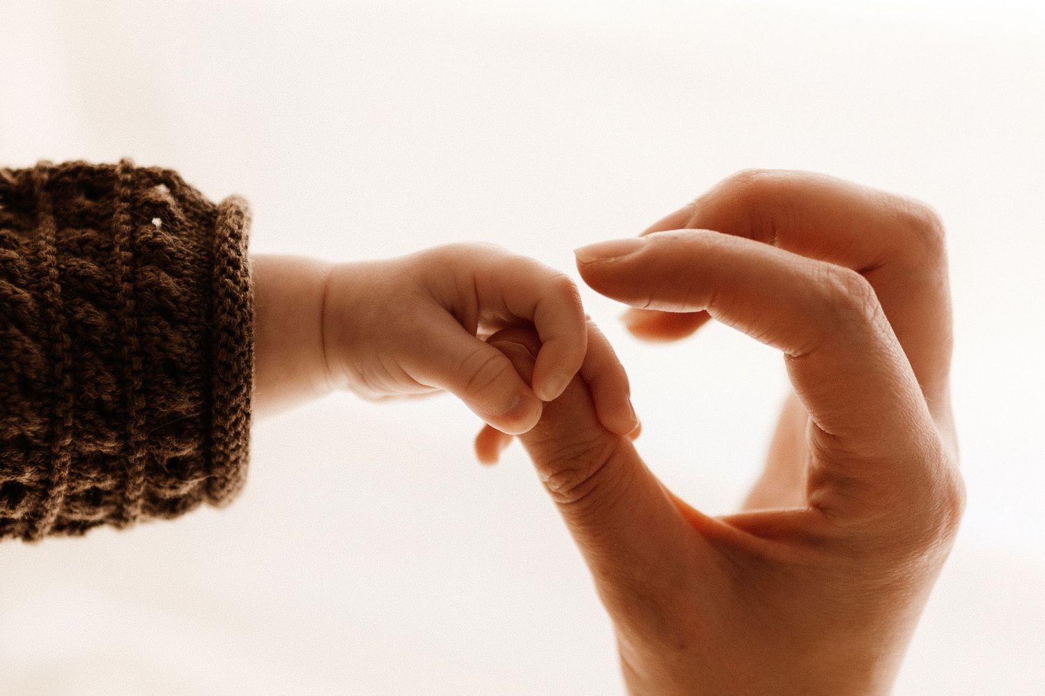 Two hands reaching towards each other against a soft backlit background.