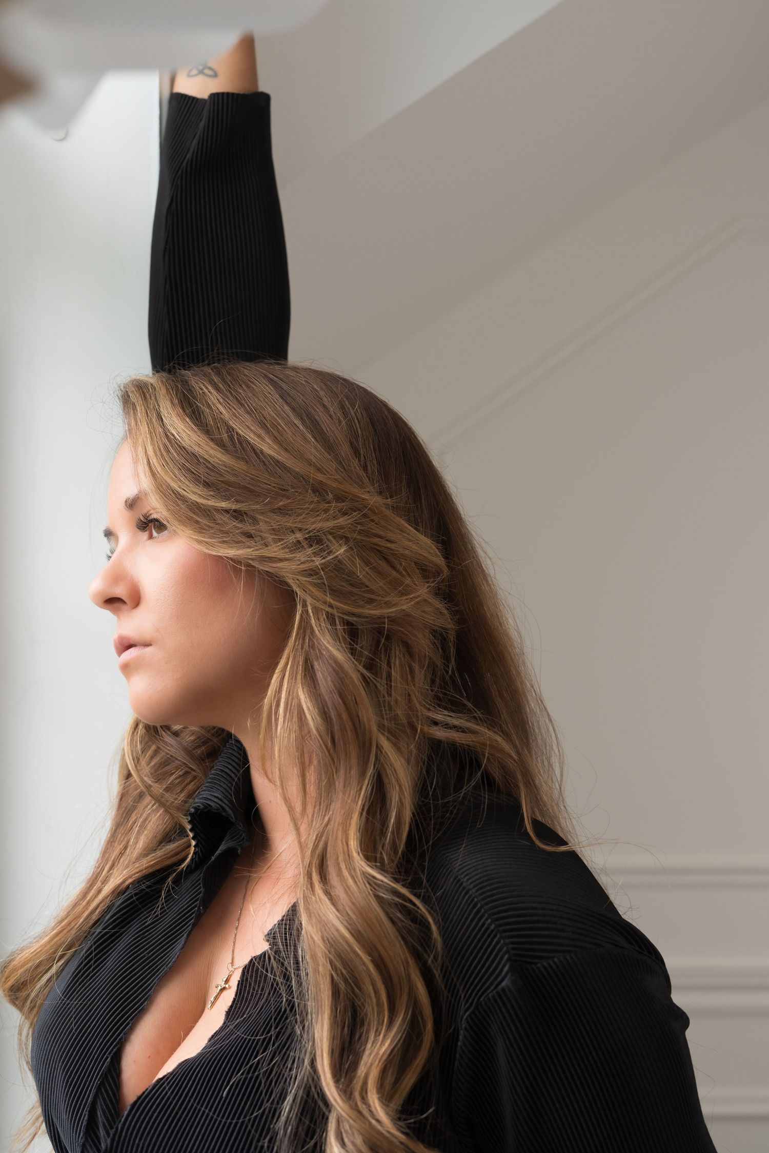 Side profile portrait with raised arm against white wall wearing black sweater.