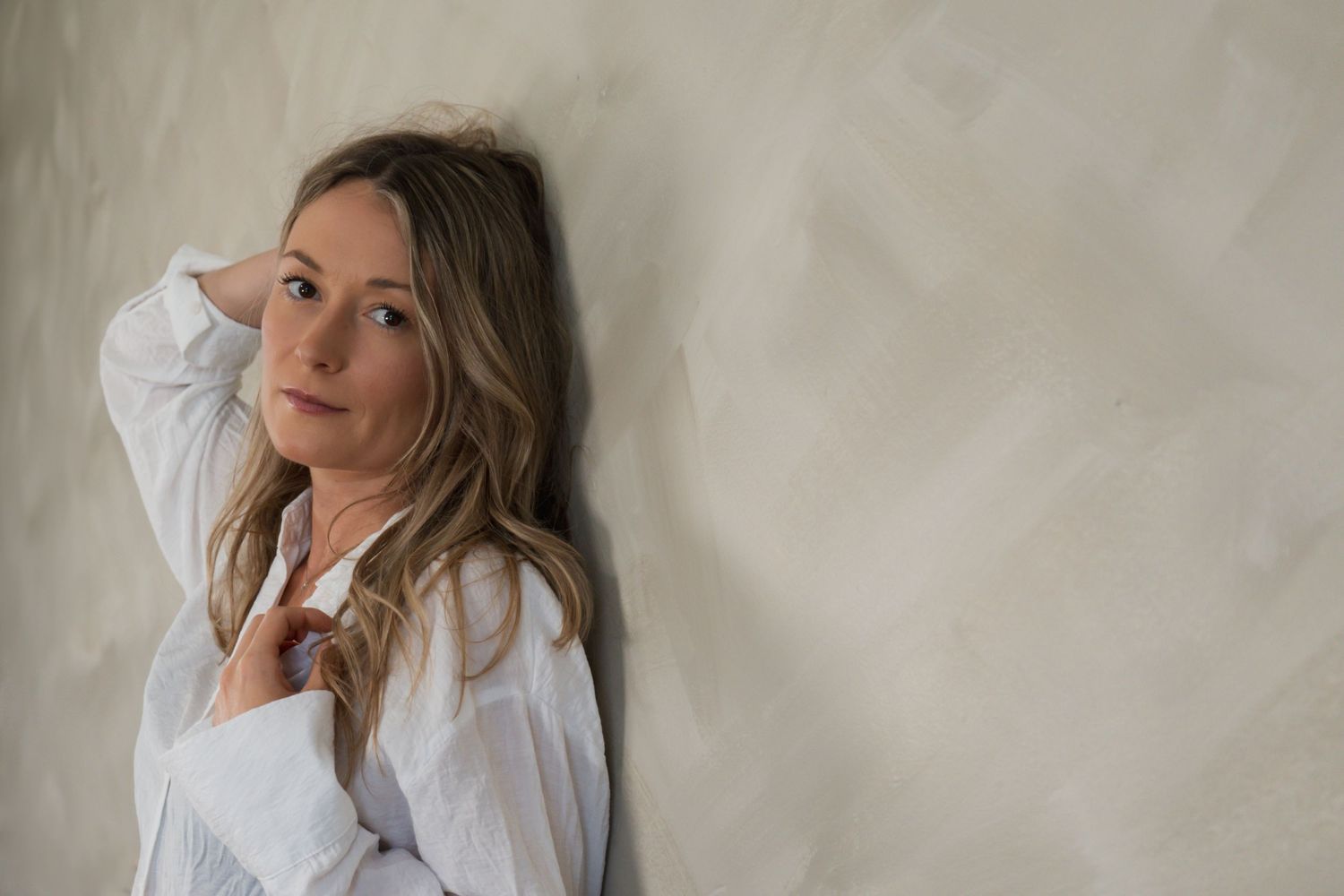 Soft portrait against white wall with person in white button-down shirt.