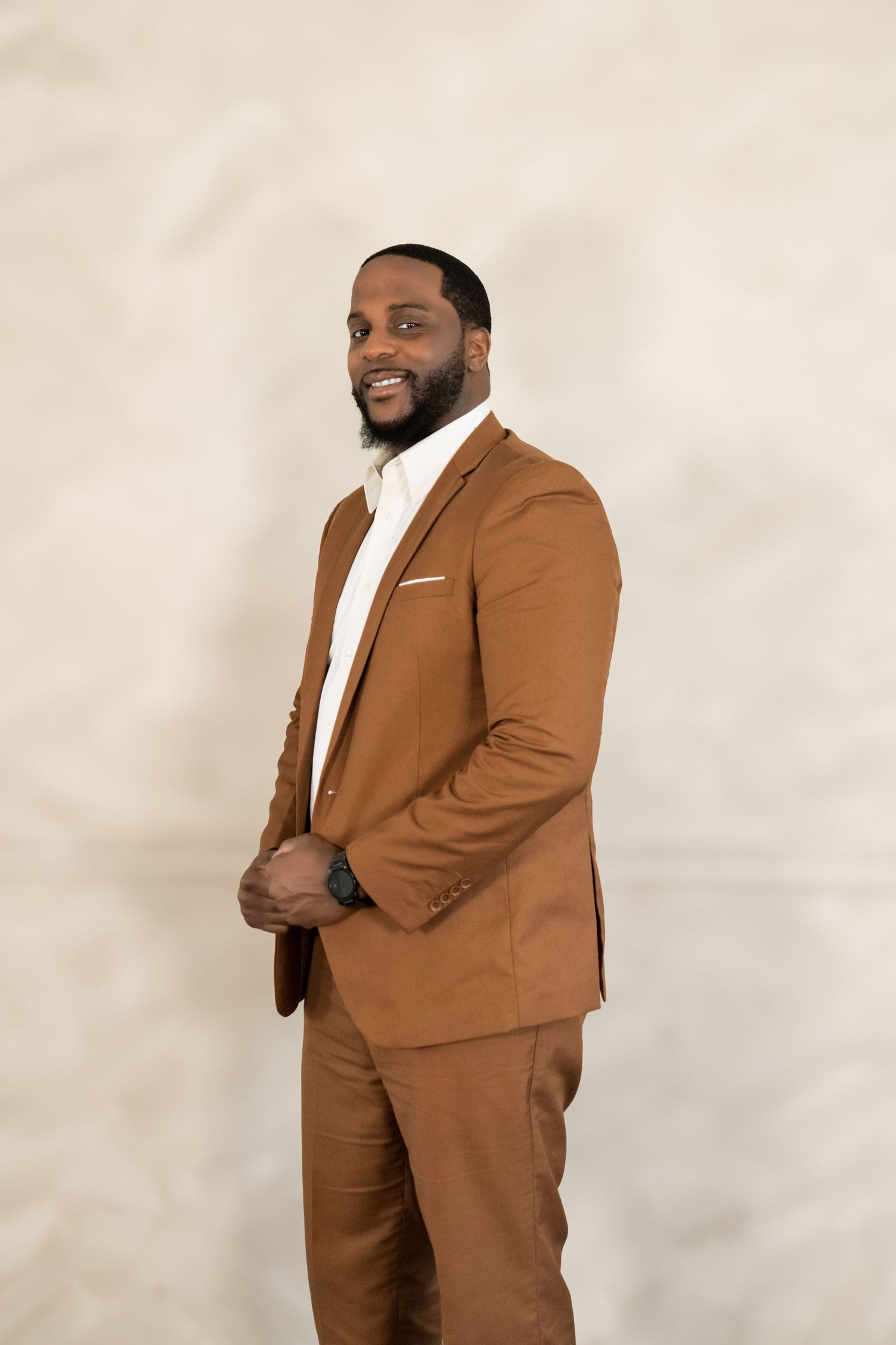 Professional portrait of person in brown suit with white shirt against neutral background.