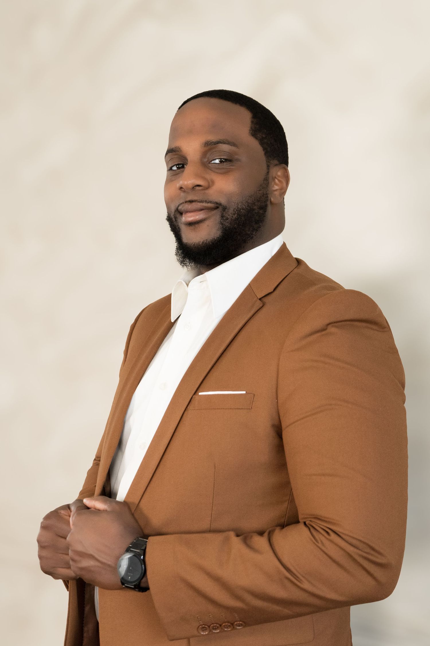Business professional in tailored brown suit poses confidently against beige backdrop.