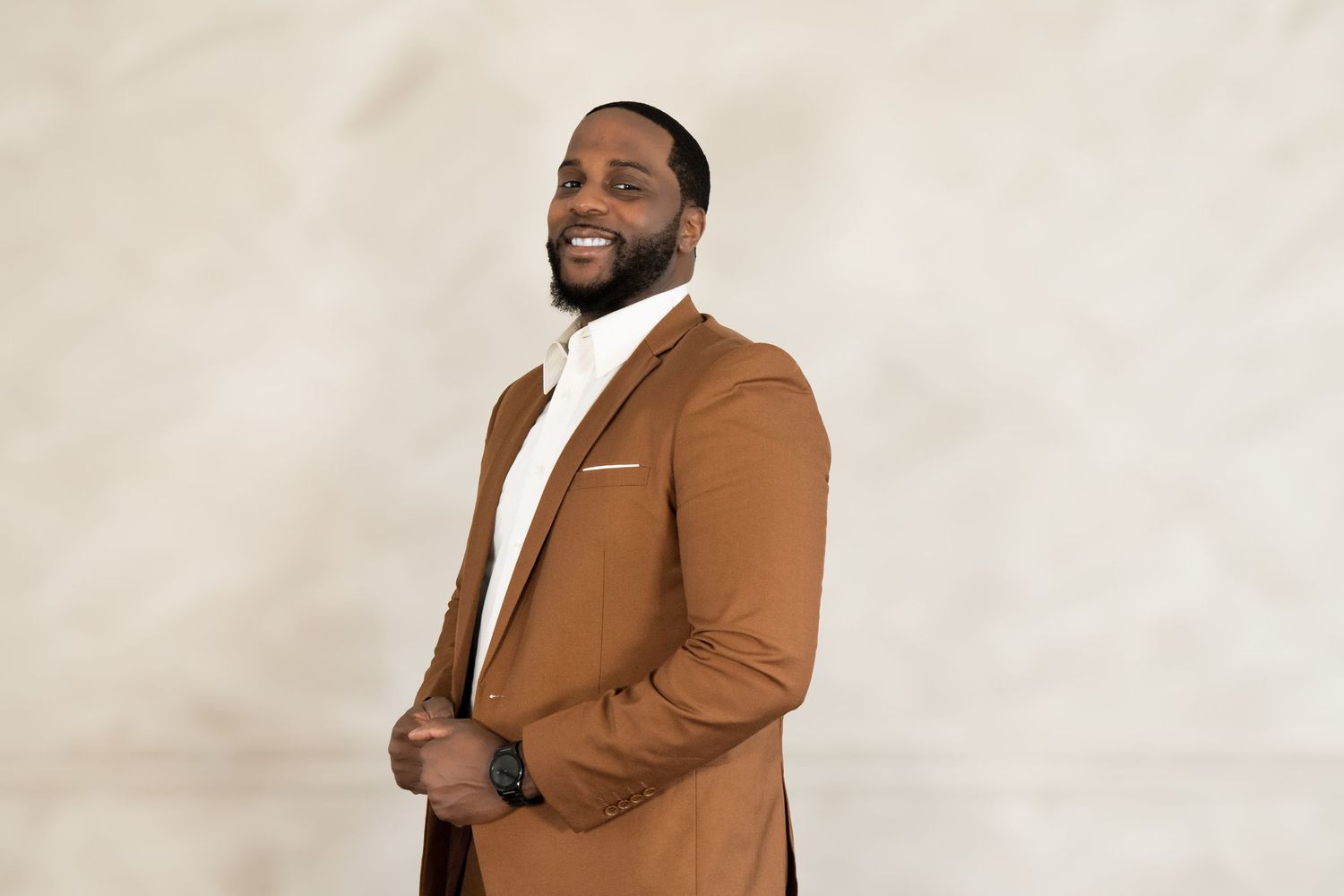 Stylish portrait of person in camel-colored suit jacket against light background.