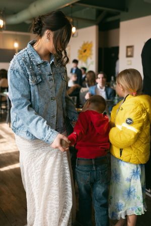 Person in denim jacket interacts with two children in a casual indoor setting illuminated with warm lighting.