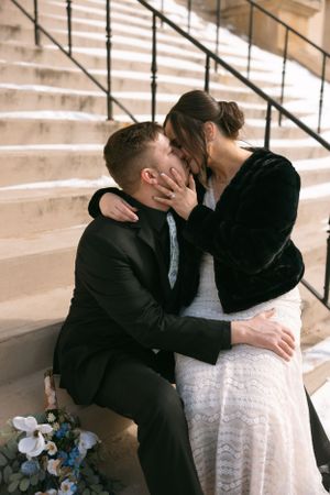 A romantic moment shared on snowy marble steps with a blue floral bouquet nearby.