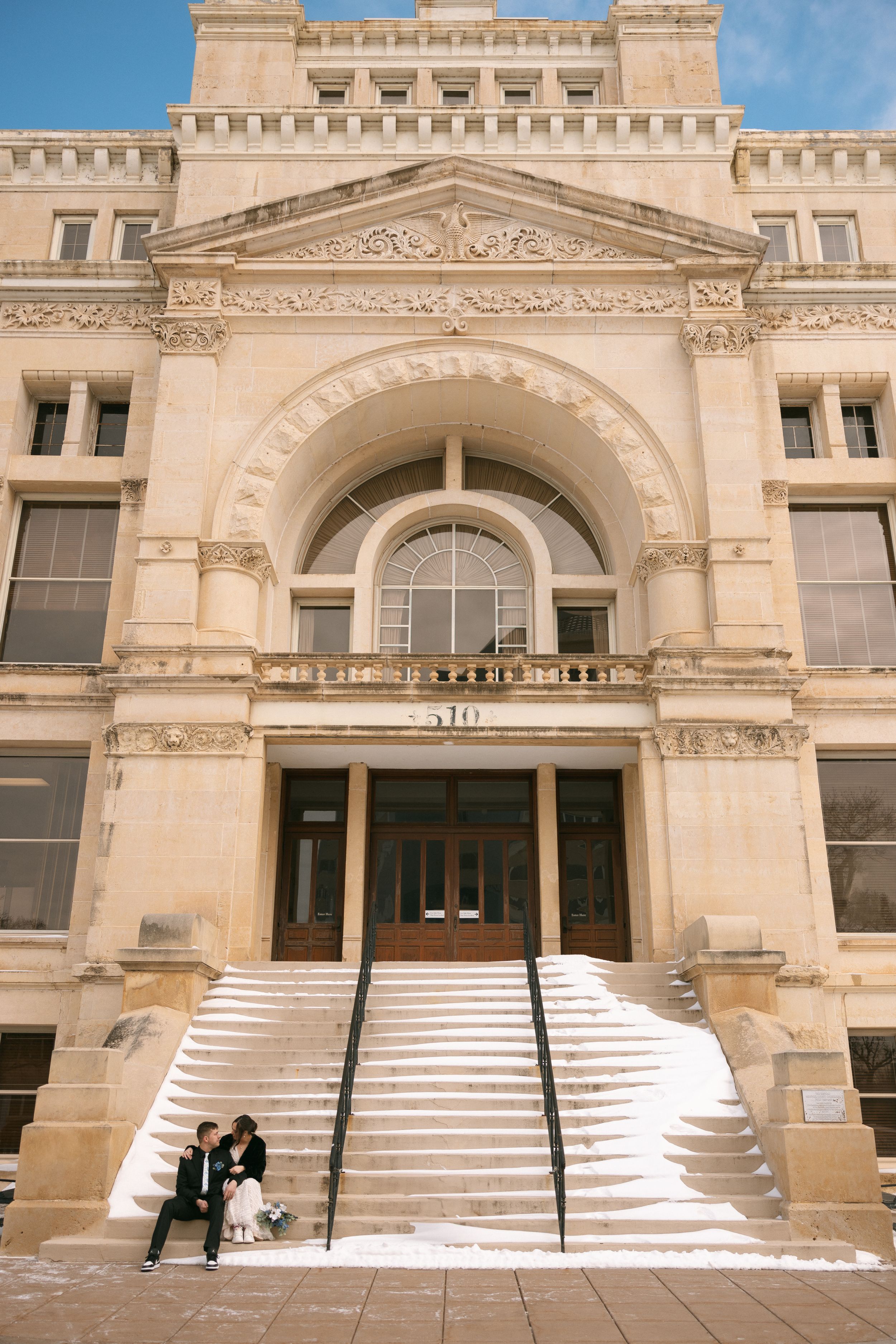 Elegant historic courthouse building with arched entrance and grand white stone staircase on a sunny day.