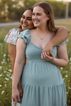 Two friends in summer dresses share a joyful moment in a wildflower meadow at sunset.