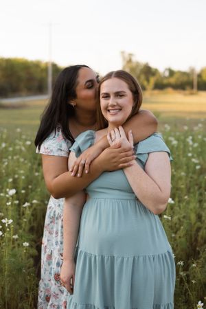 Friends sharing a warm embrace while standing in a field of wildflowers at golden hour.