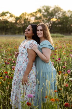 Friends in complementary dresses pose back-to-back in a vibrant flower field.