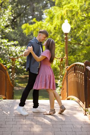 Romantic dance pose on a decorative bridge surrounded by lush spring greenery.