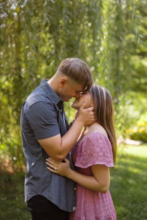 Intimate moment shared between couple under willow trees in summer garden.