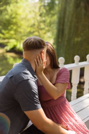 Tender embrace on white bench with sunlit greenery in background.