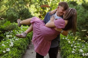 Romantic couple embracing in a garden with white flowers on a sunny day.