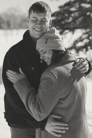 Black and white portrait of couple embracing and laughing in winter scene.