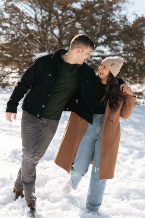 Playful winter scene with couple laughing together in snow wearing casual attire.