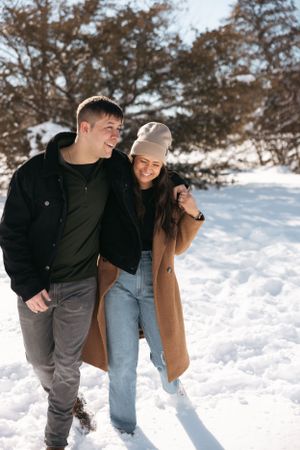 Candid moment of couple walking together in snowy landscape wearing winter clothing.