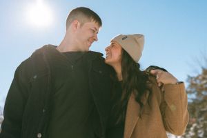 Sun-lit outdoor portrait of couple sharing joyful moment in winter setting.