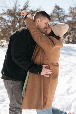 Intimate moment of couple embracing in winter scene wearing matching camel and black coats.