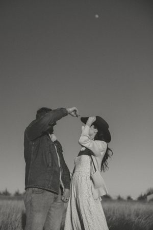 A romantic black and white photo of two people drinking from glass bottles together in a grassy field.