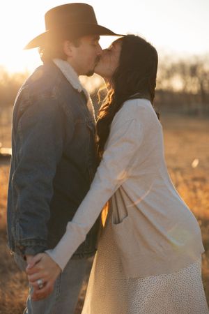 A romantic couple sharing a tender kiss at sunset in a field, backlit by warm golden light.