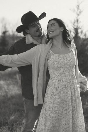 Black and white romantic portrait of couple embracing outdoors, with her in polka dot dress and him in cowboy hat.