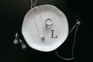 White ceramic plate with jewelry items and letter L monogram displayed on dark background.