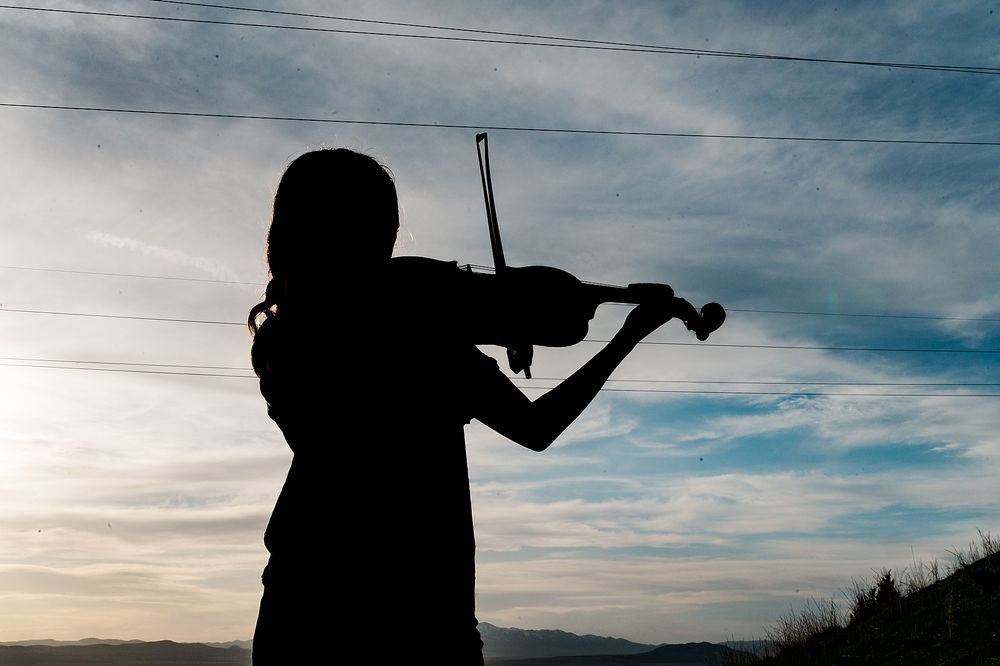 Silhouette of a violin player against a dramatic sunset sky.
