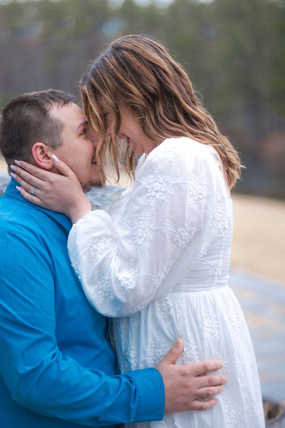 Romantic couple shares tender kiss during lakeside engagement photoshoot.