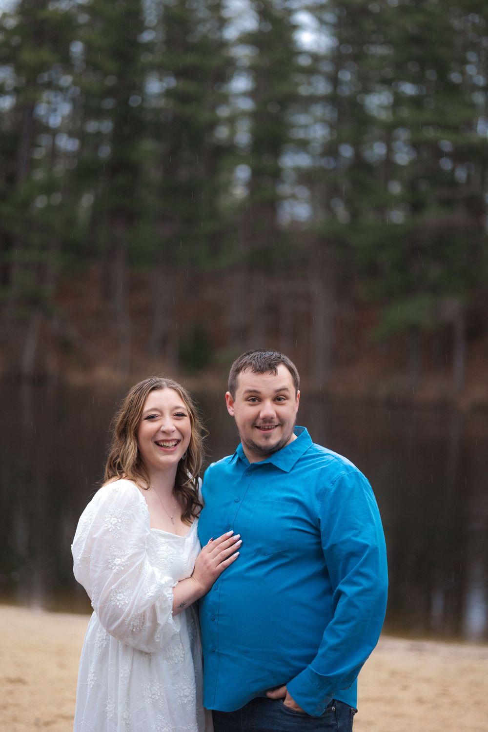 Couple poses together in casual engagement photos with pine forest backdrop.
