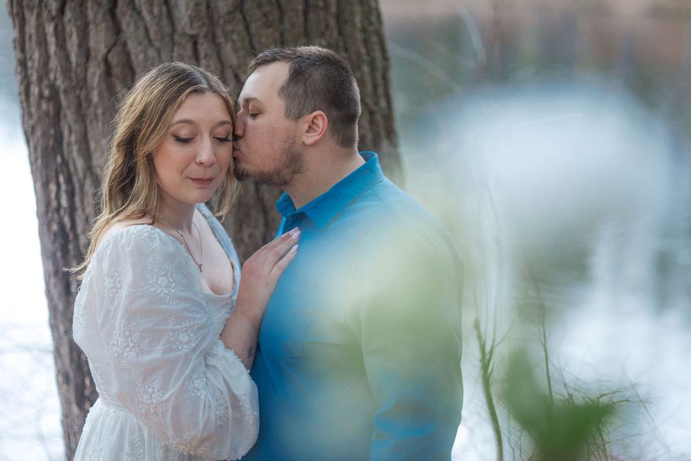 Intimate moment between couple leaning against tree during outdoor portrait session.