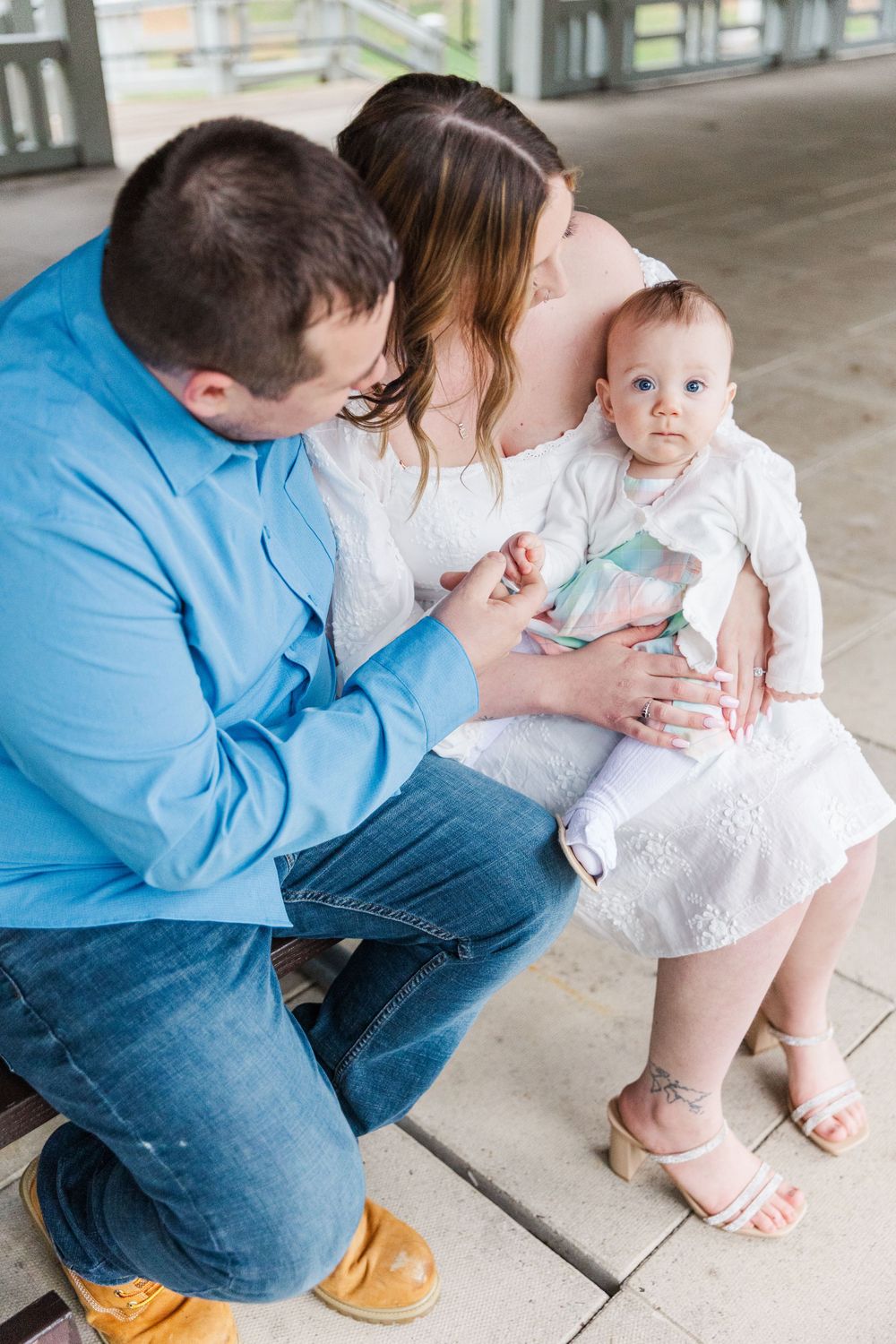 Family of three sits together on covered porch wearing coordinating blue and white outfits.