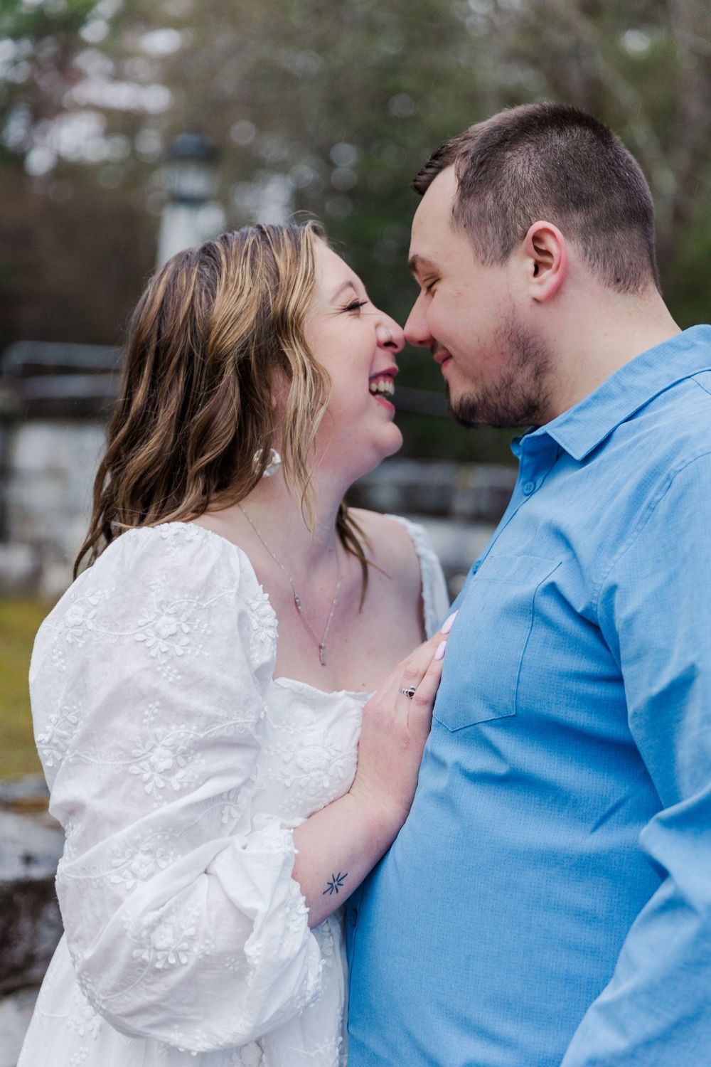 Couple in blue shirt and white dress share intimate laughing moment outdoors.