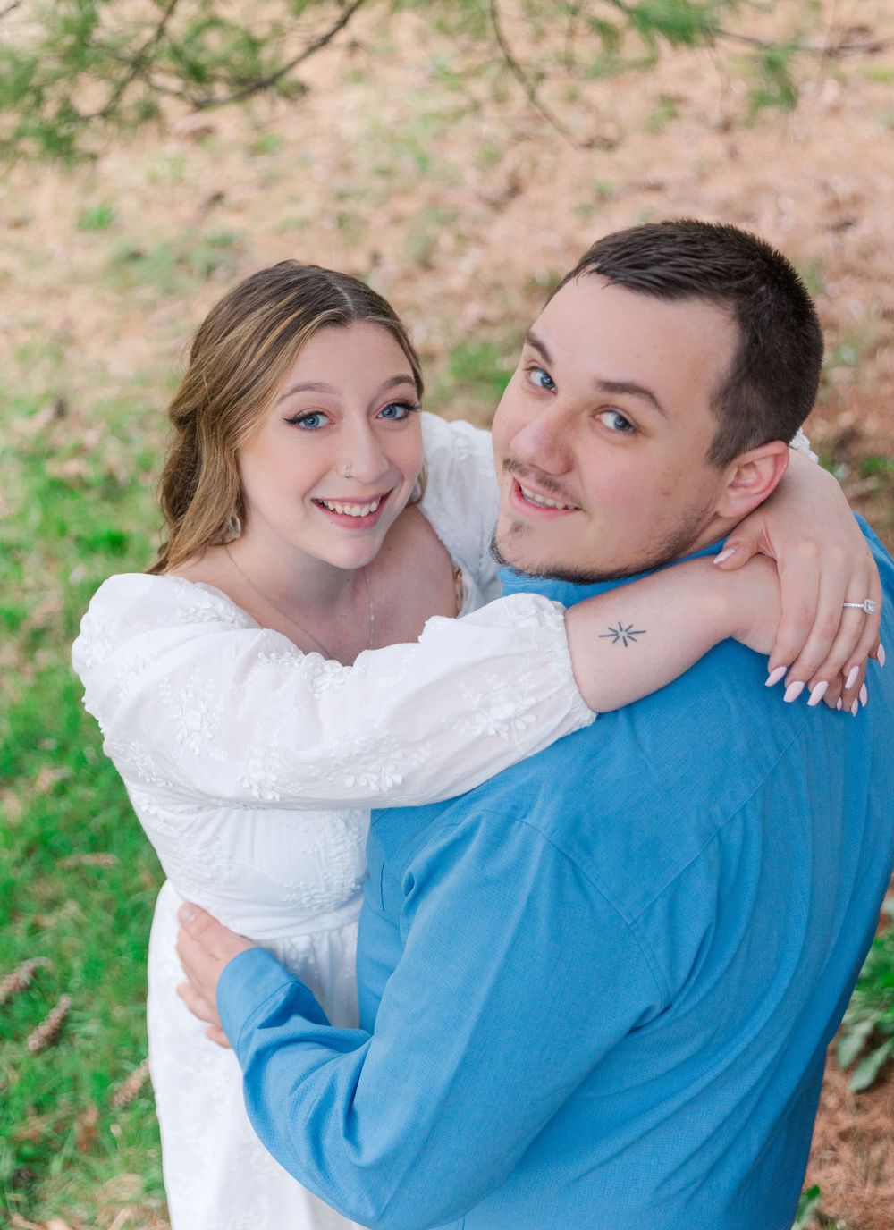 Romantic couple embrace outdoors wearing white dress and blue sweater during spring photoshoot.