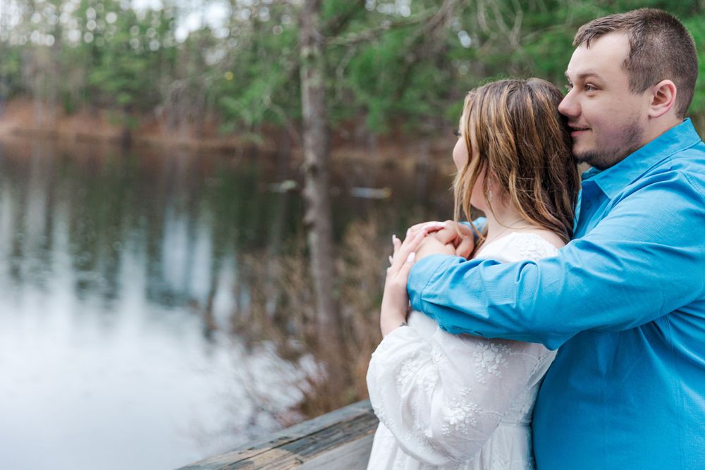 Couple embraces by lakeside during romantic outdoor photo session.