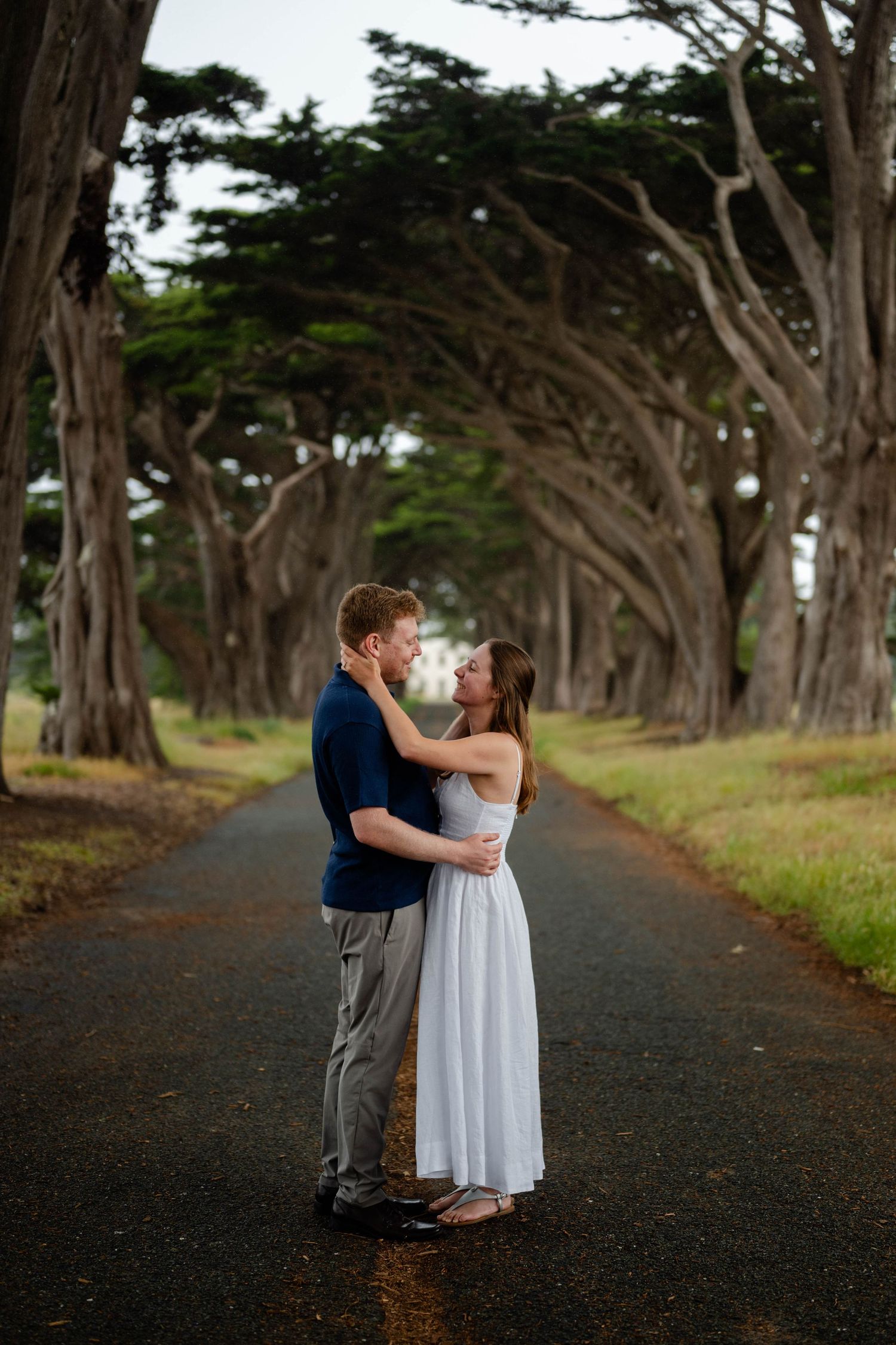A couple shares a romantic moment on a tree-lined path during an outdoor engagement photo session.