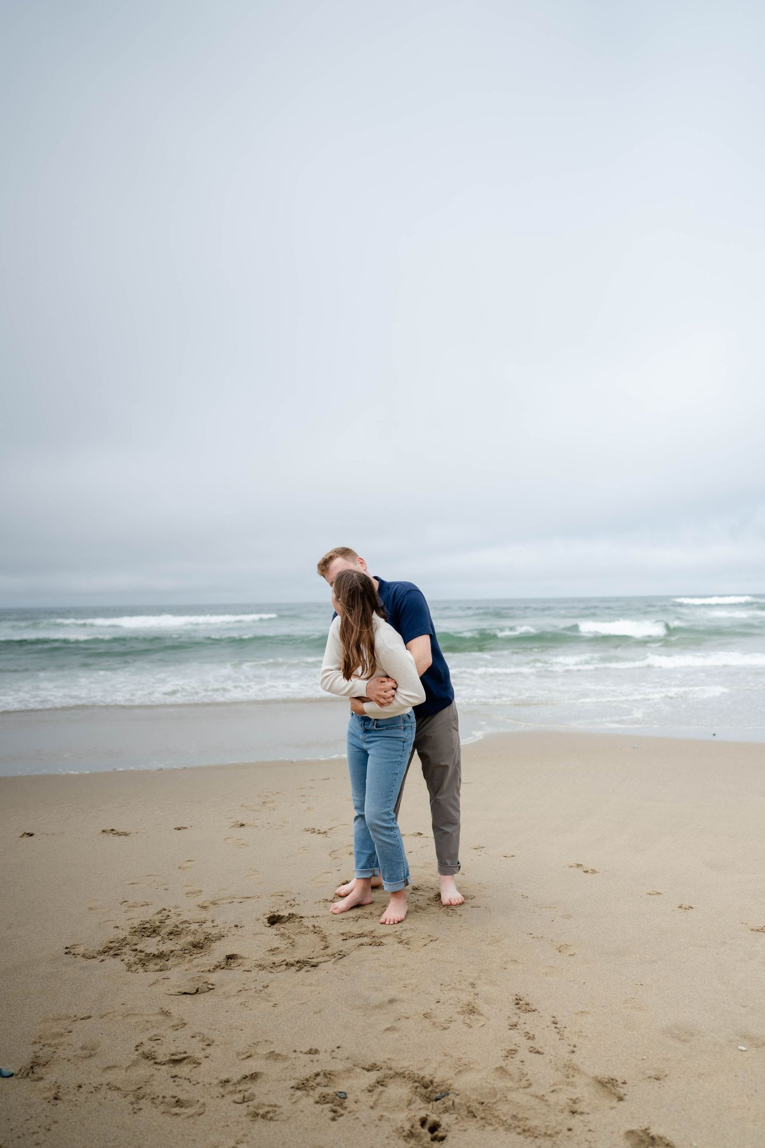 Couple embracing each other both smiling with rolling waves behind them.