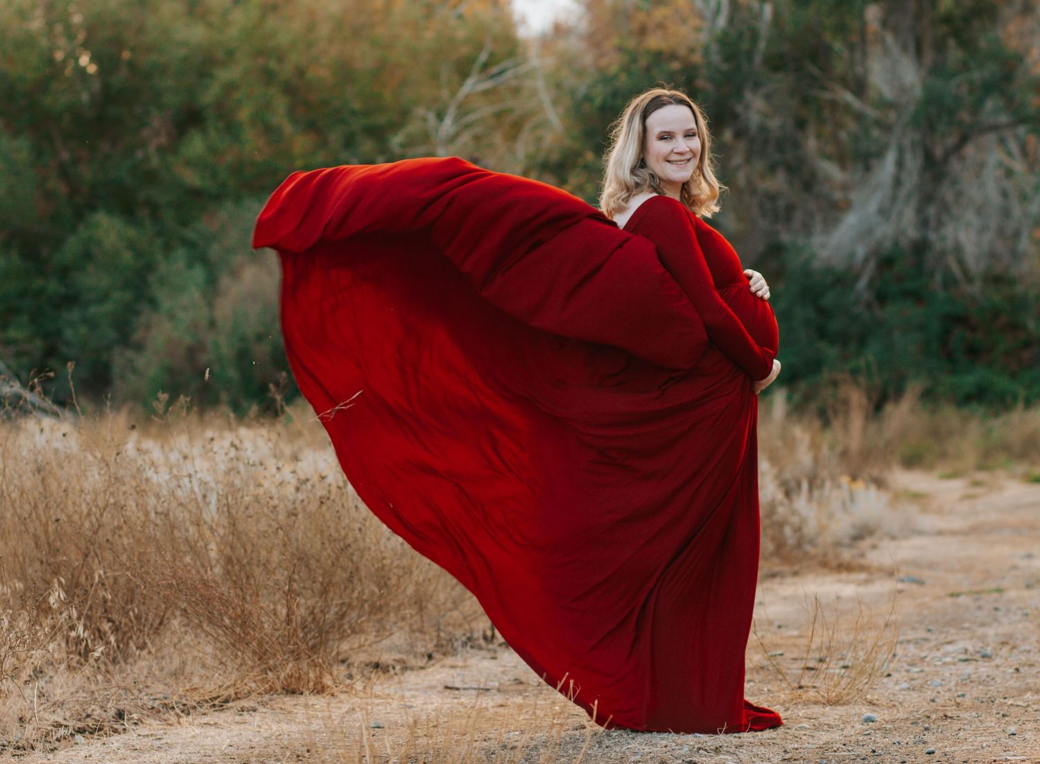 Flowing red dress twirling dramatically against fall landscape for a maternity photo session in Kennewick, Washington.