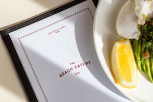 A restaurant menu with "The Beach Eatery" branding on a table with plated food.