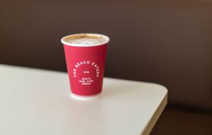 Red coffee cup with The Beach Eatery logo on white surface.