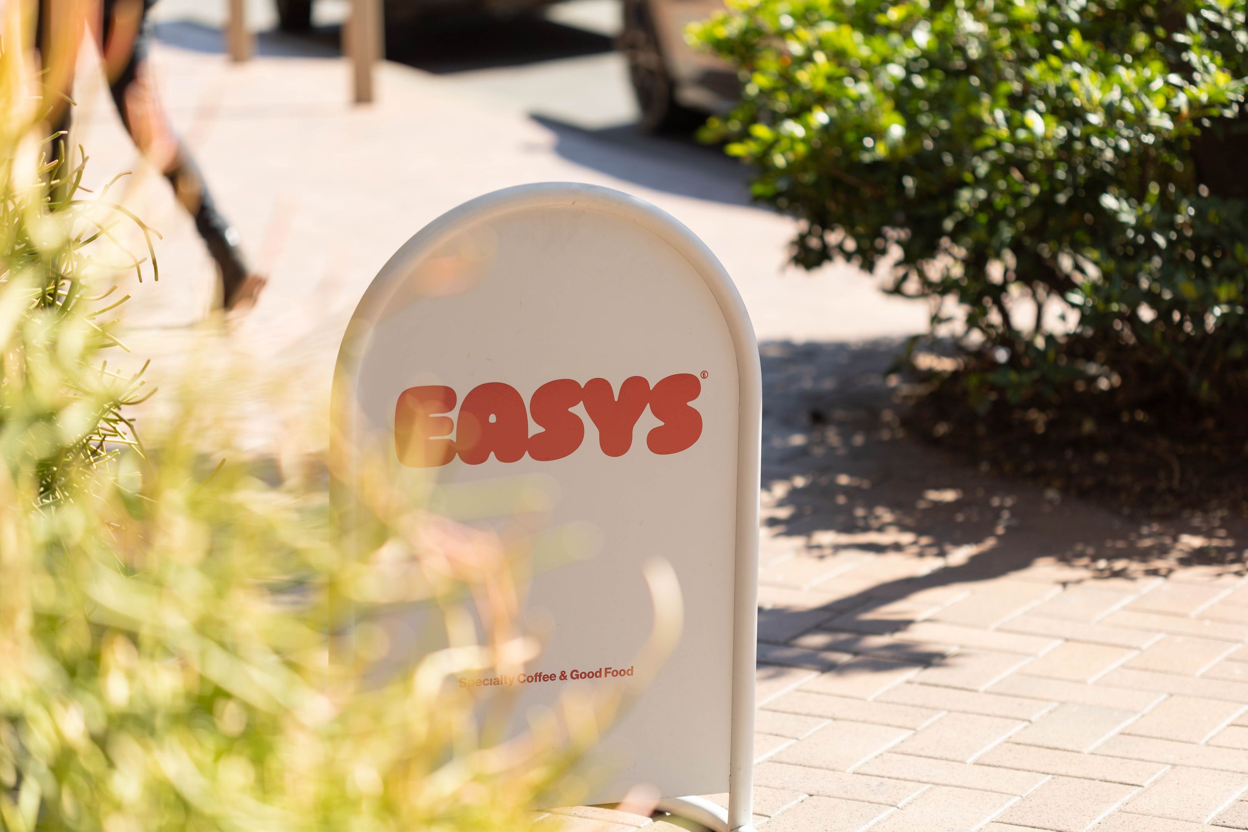 Outdoor signage for Easy's restaurant on a sunny day, surrounded by lush greenery and brick pavement.