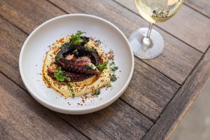 Grilled octopus on creamy hummus with herbs and spices, served with white wine on a rustic wooden table.