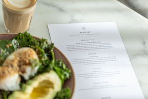 A Tuesday cafe menu beside a fresh salad with avocado and poached eggs, with a latte in the background.
