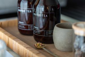 Two dark glass bottles of tea with a ceramic cup on a wooden surface.