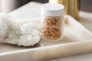 Clear The Tenth supplement bottle with capsules on white marble tray next to crystal cluster.