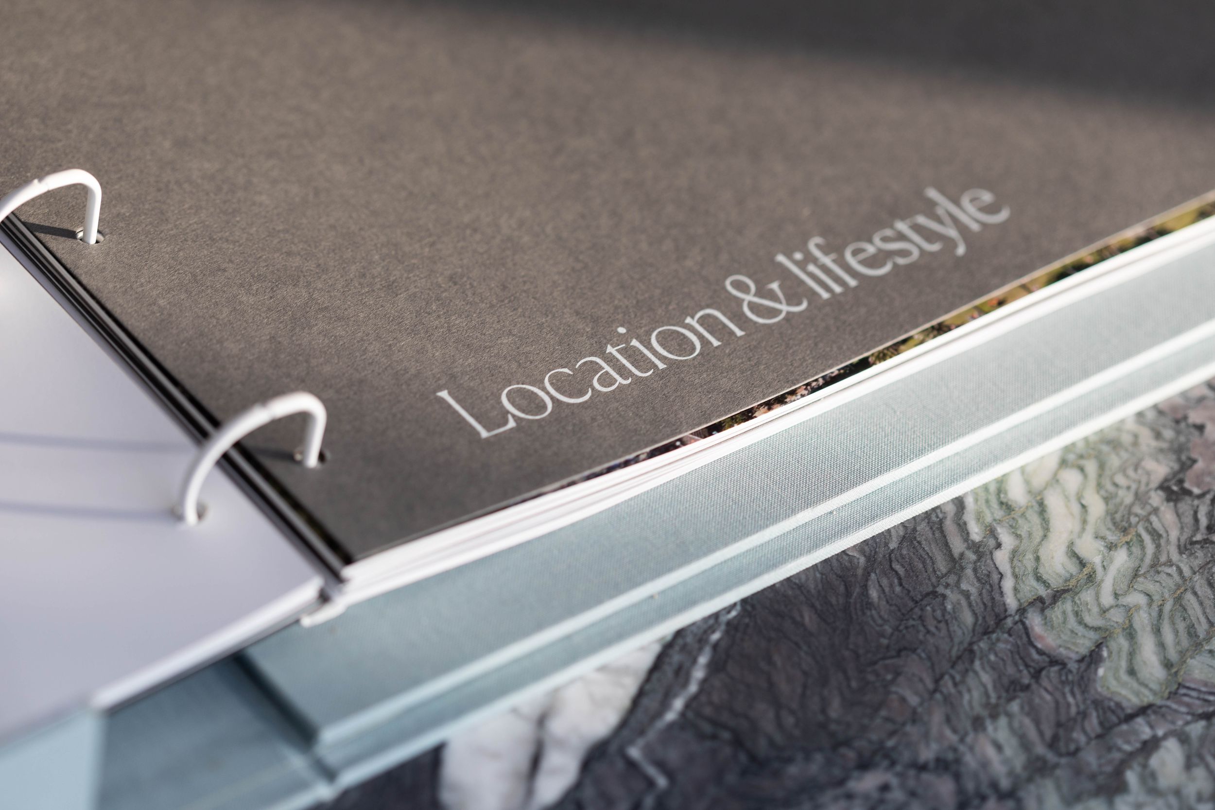 Close-up of a gray binder with silver rings labeled Location & lifestyle, partially open with documents inside.