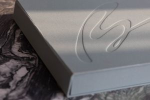 Elegant silver gift box with embossed cursive logo resting on dark marble surface.