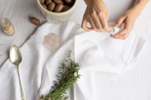 Overhead view of table setting with fresh herbs, cork, and hands folding white linens.